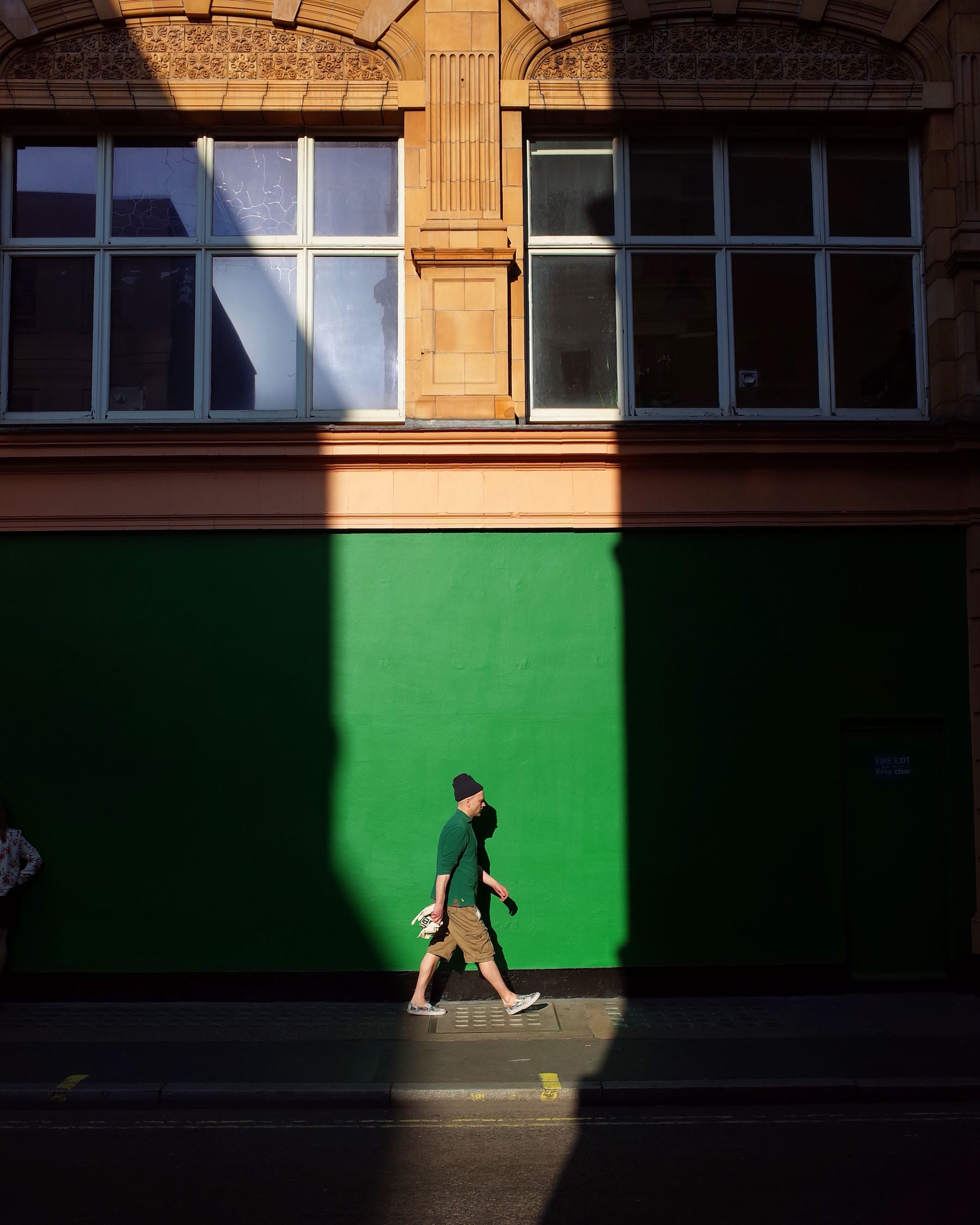 A person walks through a shaft of sunlight against a green wall.